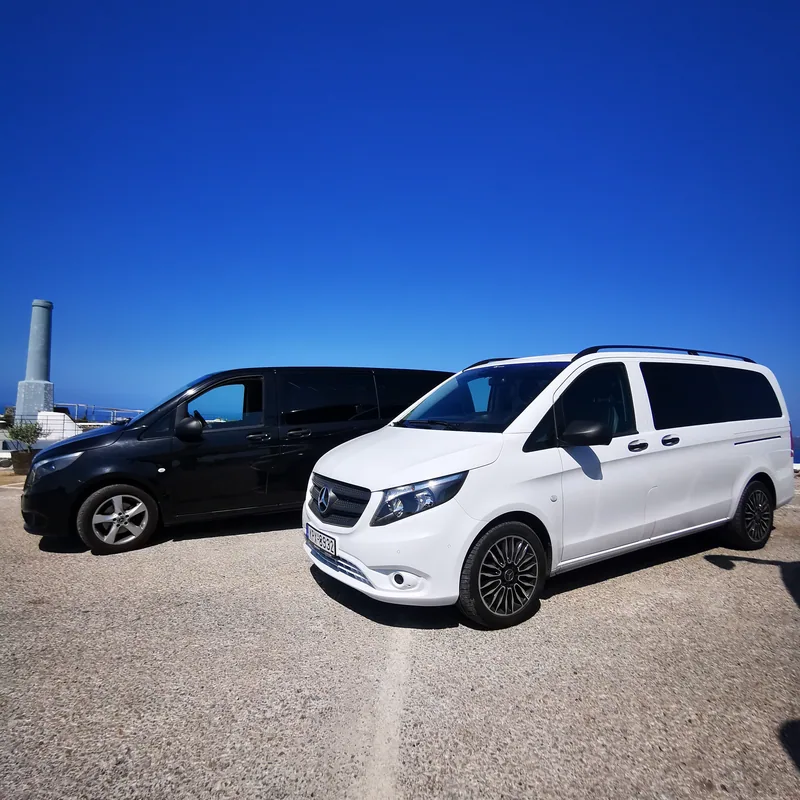 The black and the white Mercedes-Benz Vito of VH Transfer parked side by side above the Santorini caldera