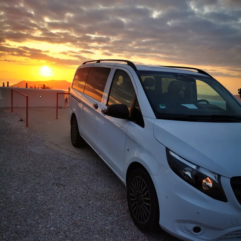A white Mercedes-Benz Vito parked at a Santorini caldera viewpoint in golden evening light